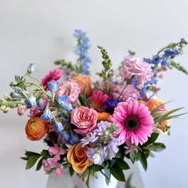 Colorful mixed bouquet in a white vase with pink, orange, blue, and purple blooms