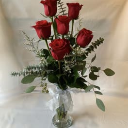 Red roses arranged in a clear glass vase with a white ribbon