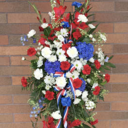 Standing floral wreath with red, white, and blue flowers on a ribboned easel