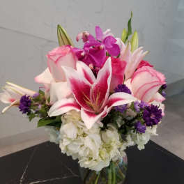 Pink lilies and roses with purple orchids in a glass vase