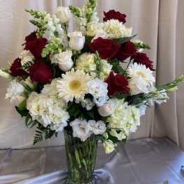 Red and white roses with white daisies in a glass vase
