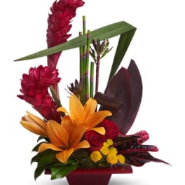 Tropical flower arrangement with orange lilies and red blooms in a red container