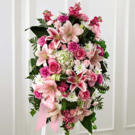 Standing spray of pink lilies, roses, carnations, and white daisies on an easel.