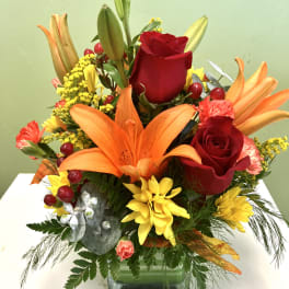 Bright mixed bouquet with red roses, orange lilies, and yellow flowers in a glass vase
