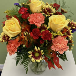 Mixed bouquet of yellow roses, carnations, and daisies in a glass vase