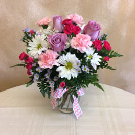 Mixed bouquet of pink and purple roses, carnations, and daisies in a glass vase