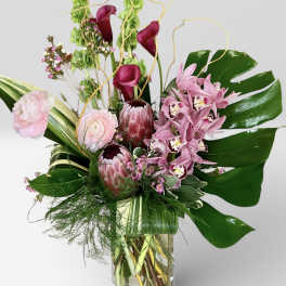 Pink orchids and calla lilies in a glass vase with tropical leaves