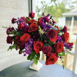 Bouquet of red roses and purple flowers in a white vase