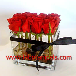 Red roses arranged in a clear square vase with a black ribbon