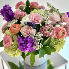 Mixed pink, purple, and green flowers arranged in a white box