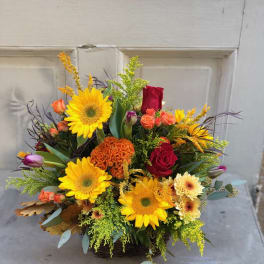 Mixed bouquet with sunflowers, red roses, and orange blooms in a basket