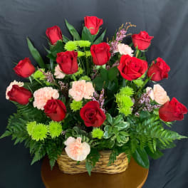Basket arrangement of red roses, pale pink carnations, and green mums