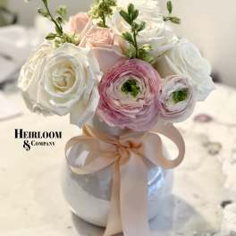 Pink and white roses with ranunculus in a white vase tied with a blush ribbon