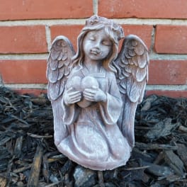 Stone angel figurine holding a heart in front of a brick wall