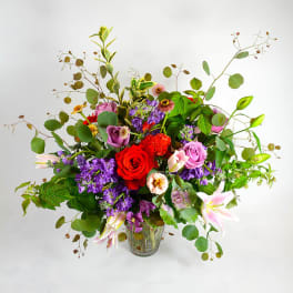 Mixed bouquet of roses, lilies, and purple flowers in a glass vase