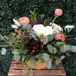 Mixed floral arrangement in an orange container with coral and white blooms