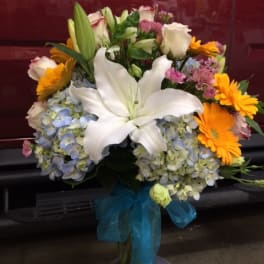 Bouquet with white lilies, blue hydrangeas, and orange daisies in a glass vase