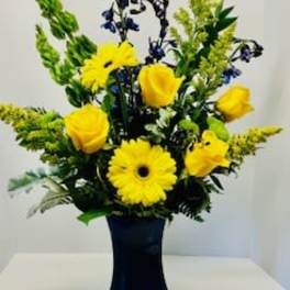 Yellow gerbera daisies and roses in a dark vase