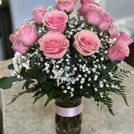 Pink roses and baby's breath in a glass vase with a pink ribbon