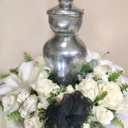 White rose arrangement around a silver urn with a black ribbon