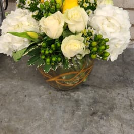 Low arrangement of white hydrangeas and roses with yellow roses in a round painted glass vase
