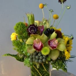 Mixed floral arrangement in a clear square vase with tall stems and round blooms