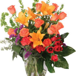 Mixed bouquet of orange lilies, roses, and red flowers in a glass vase