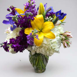 Bouquet of yellow lilies, purple flowers, and white blooms in a glass vase