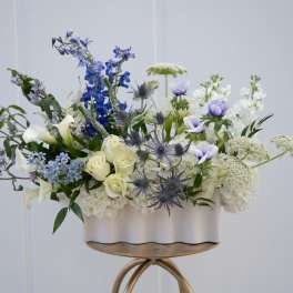 Blue, white, and cream floral arrangement in a white container