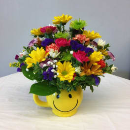 Colorful mixed flower arrangement in a yellow smiley-face mug