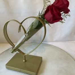 Two red roses in a clear cone vase on a gold heart stand
