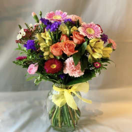 Mixed bouquet of pink, orange, yellow, and purple flowers in a glass vase