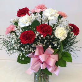Bouquet of red, white, and pink carnations in a glass vase with a pink ribbon