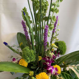 Tall tropical arrangement with purple orchids and yellow blooms in a vase