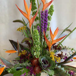 Tropical arrangement with orange bird-of-paradise and purple orchids in a white vase