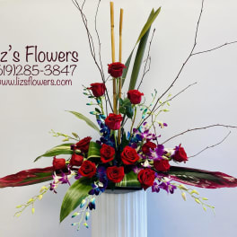 Tall arrangement of red roses and purple orchids in a white pedestal vase