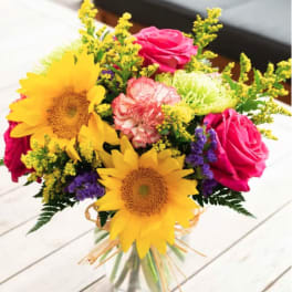 Bouquet of sunflowers, pink roses, and mixed filler flowers in a glass vase