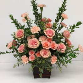 Pink roses and peach carnations arranged in a dark wooden container
