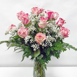 Tall clear vase of pink-tipped white roses with small white filler flowers.