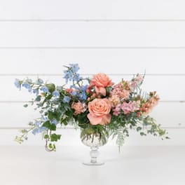 Peach roses and blue flowers in a clear glass vase