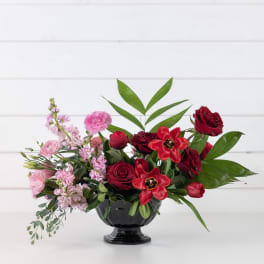 Red and pink floral arrangement in a black pedestal vase