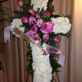 White floral cross with pink roses and ribbon on an easel