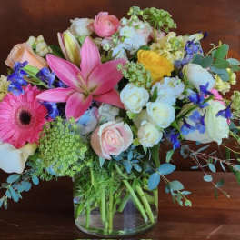 Mixed bouquet of pink, white, yellow, and blue flowers in a glass vase