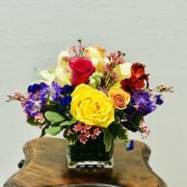 Colorful bouquet of roses and mixed flowers in a square glass vase
