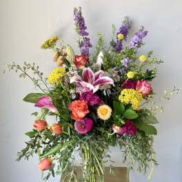 Mixed bouquet with lilies, roses, tulips, and purple spikes in a glass vase