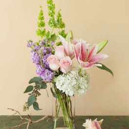 Pink lilies, roses, hydrangea, and purple stock in a glass vase
