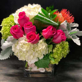 Bouquet of hot pink roses, white hydrangeas, and orange tropical blooms in a vase