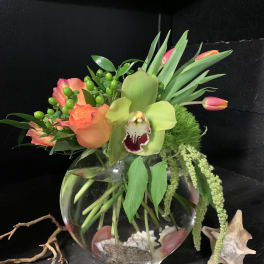 Tropical floral arrangement in a round glass vase with orchids and tulips