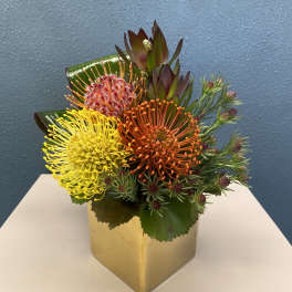 Bright mixed bouquet in a gold square vase with yellow and orange blooms