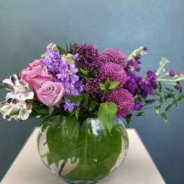 Pink and purple flowers arranged in a round glass vase